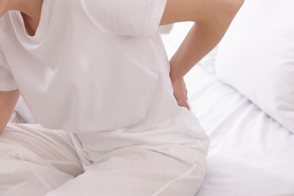 Frau sitzt im Bett und greift an die Hüfte wegen Hüftschmerzen