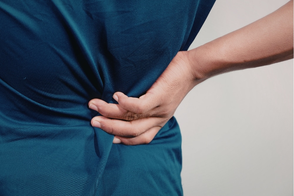 Nahaufnahme: Hand greift an den unteren Rücken bei Schmerzen